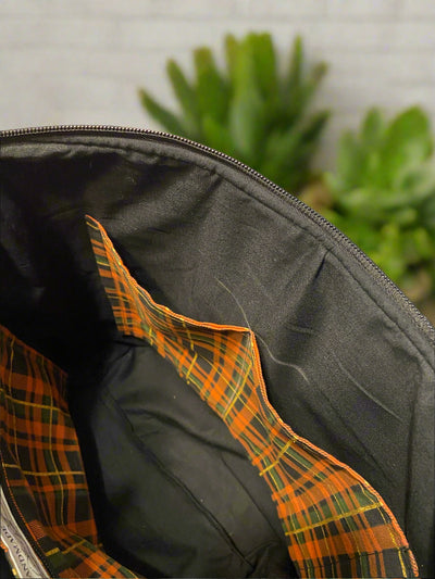 Close up of interior of tote bag black cotton lining, with open plaid pockets on one side and open/zipper pocket on the other side.